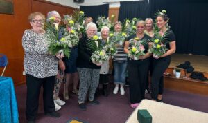 A small group of women stood together holding small floral arrangements they have made.